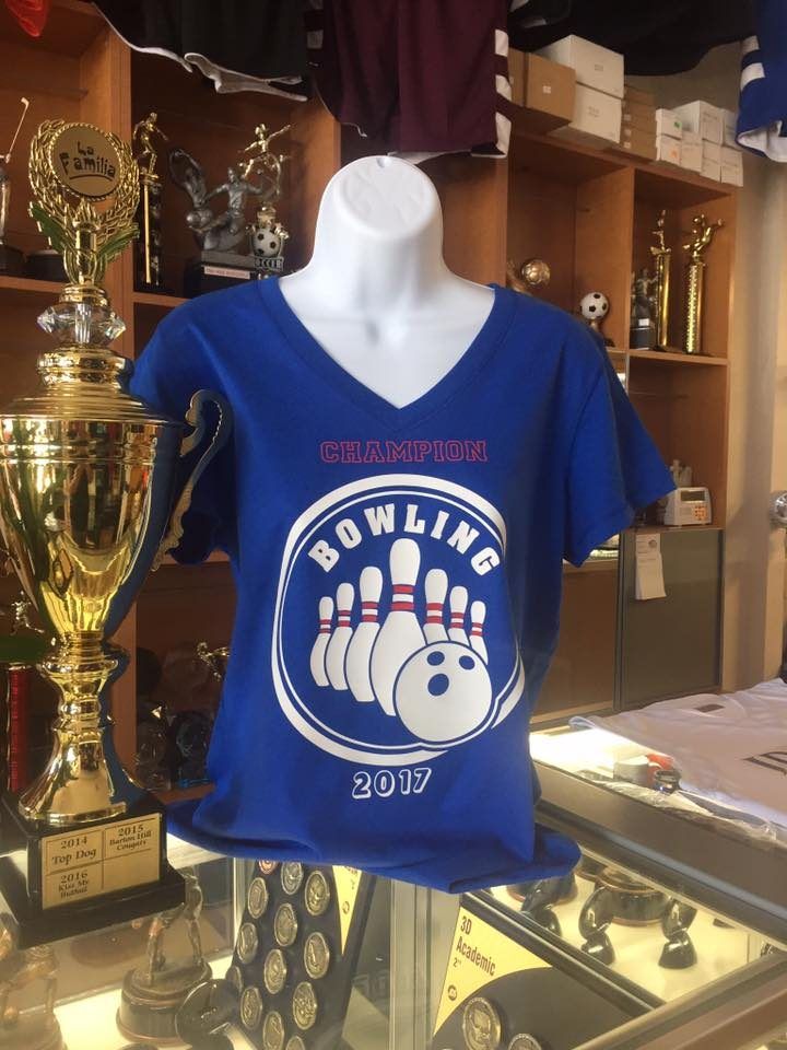 A royal blue v-neck tee printed Champion Bowling 2017 with pins and a ball, beside a gold cup trophy