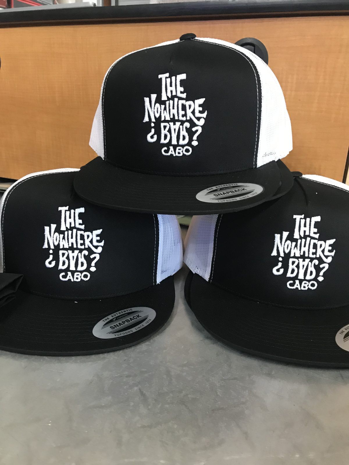 Three black snapback trucker caps with white mesh backs, embroidered in white with a Cabo bar’s lettered logo