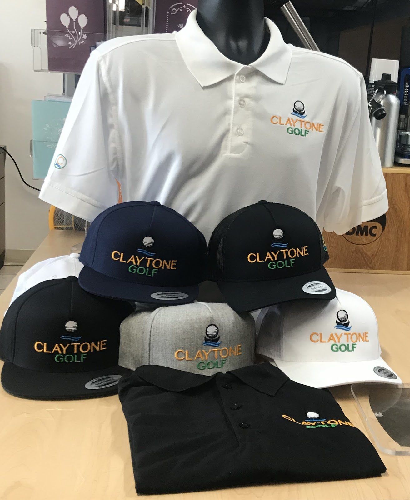 White and black polos and five caps in black, navy, gray and white, all embroidered with the Claytone Golf logo in orange and green