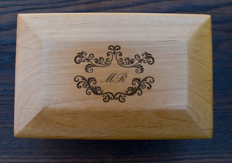 The lid of a light wooden box engraved with the monogram MR inside ornate scrollwork