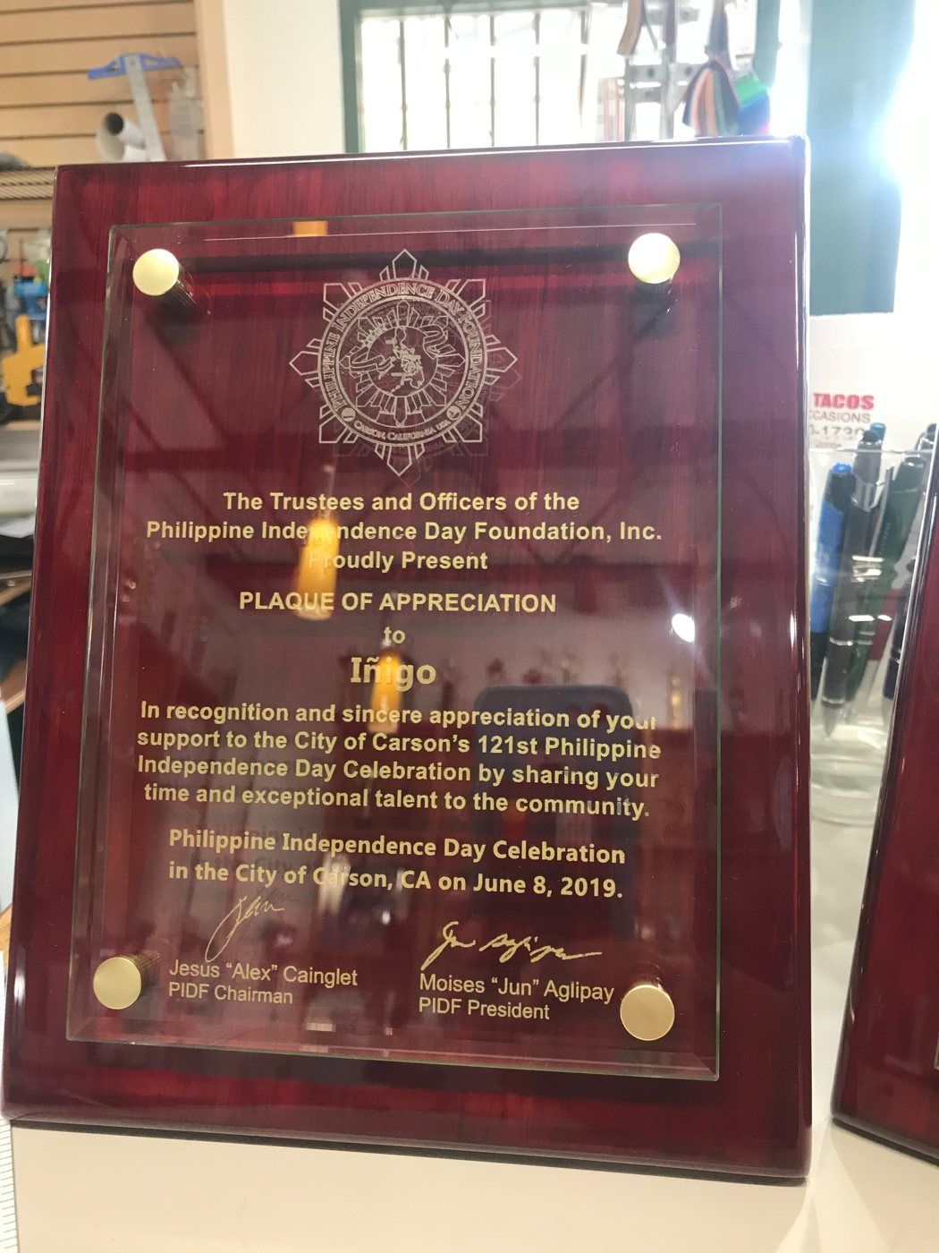 A red piano-finish plaque with a clear glass plate on brass standoffs, engraved and filled in gold: a plaque of appreciation from the Philippine Independence Day Foundation in Carson