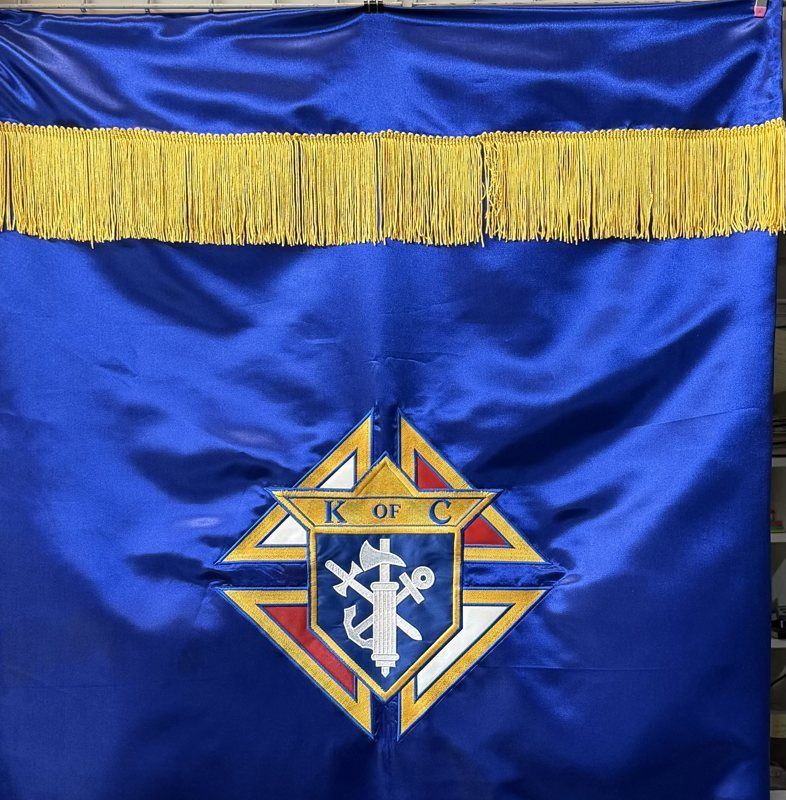 The top of a royal blue satin banner: gold fringe above the Knights of Columbus emblem in tackle twill