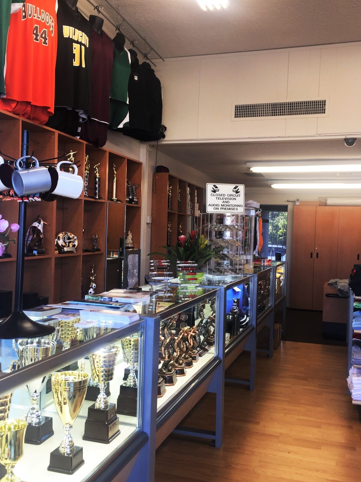 Inside our shop: lit glass counters of cup trophies and figures, maple shelves of awards, and team jerseys hanging above